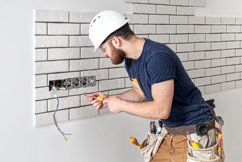 Electrician construction worker with a beard in overalls during the installation of sockets. Home renovation concept.